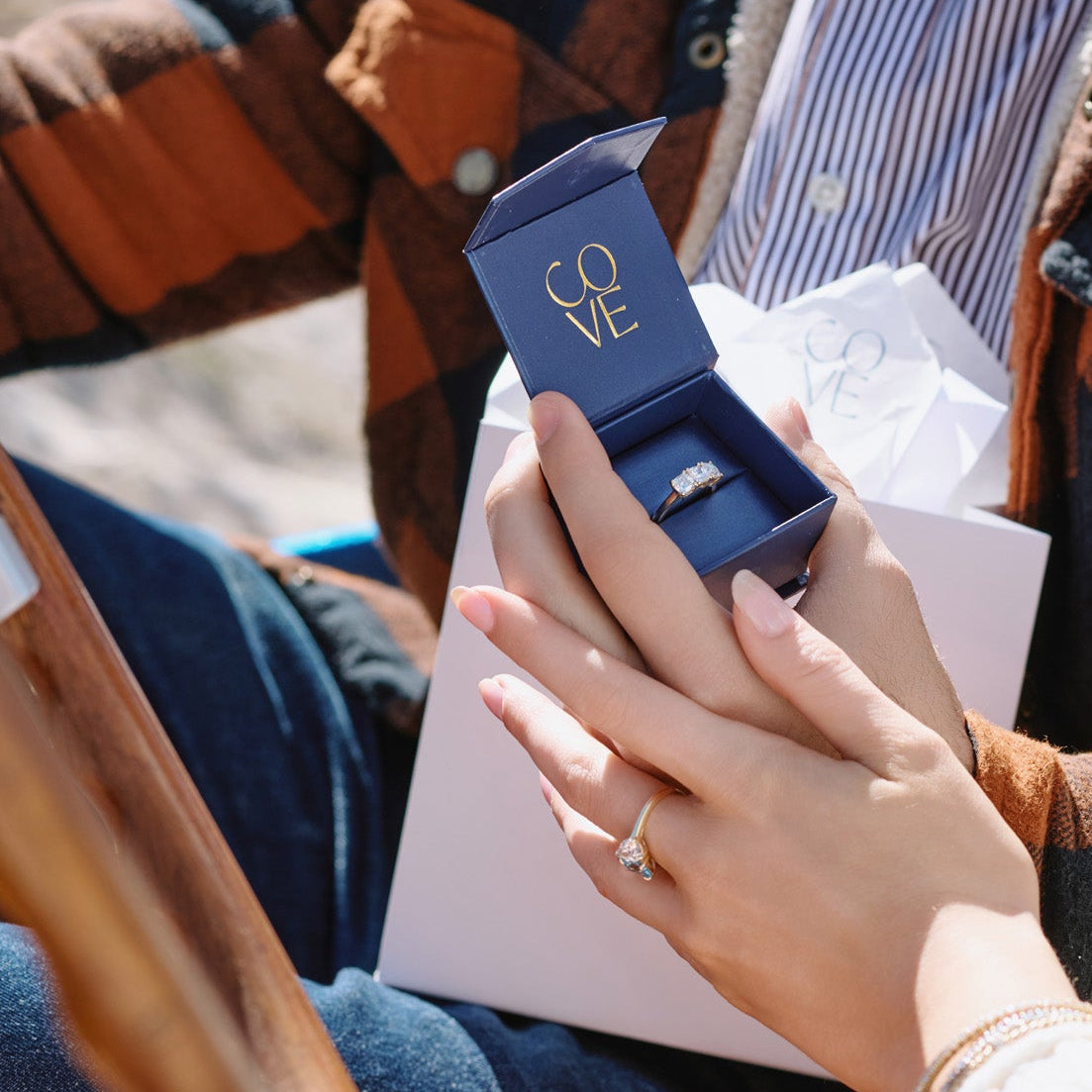 Woman opening a box with a 3 stone anniversary diamond ring in cushion cut