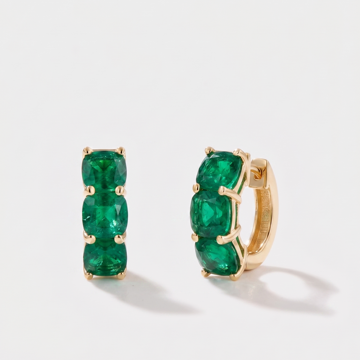 Close-up of cushion cut emerald hoop earrings on ear in 14k gold