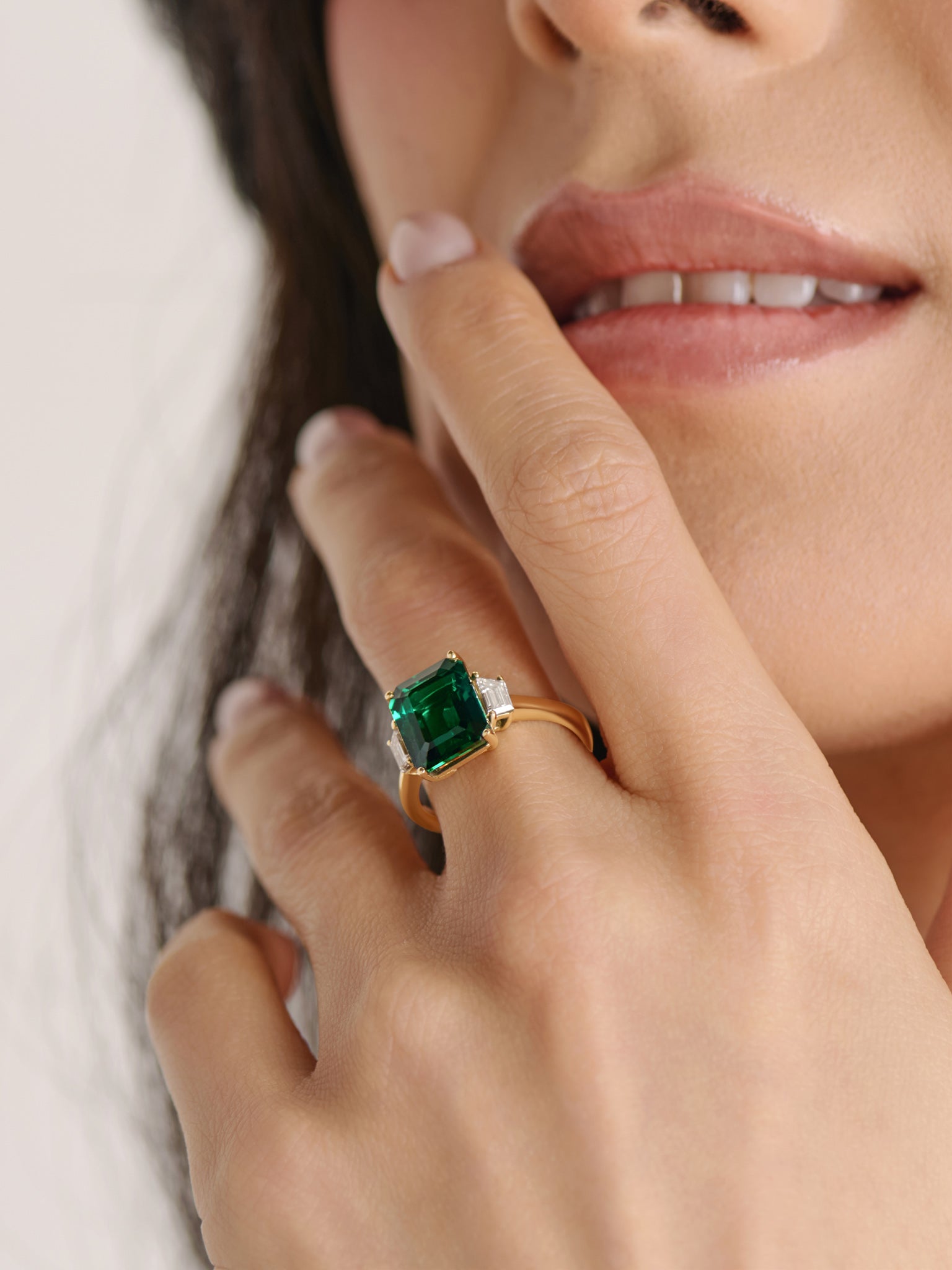 Model wearing a lab-grown emerald cut three-stone diamond engagement ring with trapezoid side diamonds designed by Cove Fine Jewelry.