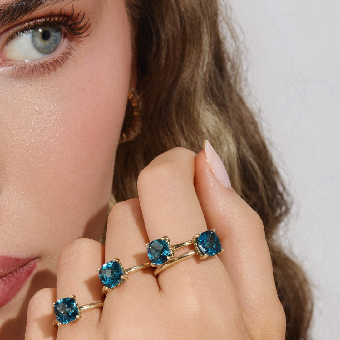 Model wearing the Hydrangea Ring featuring an AAA checkerboard-cut London Blue Topaz center stone surrounded by a halo of green diamonds in solid gold by Cove Fine Jewelry
