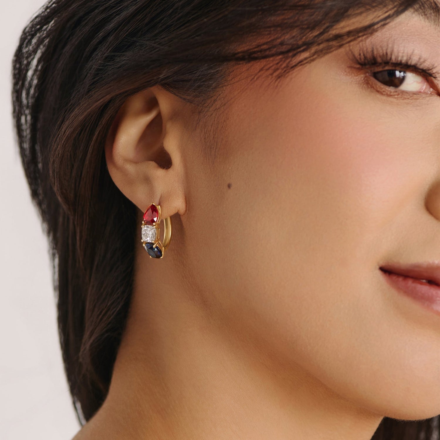 Model wearing solid white gold gemstone hoop earrings featuring red ruby, white diamond, and blue sapphire stones from the America250 fine jewelry collection.