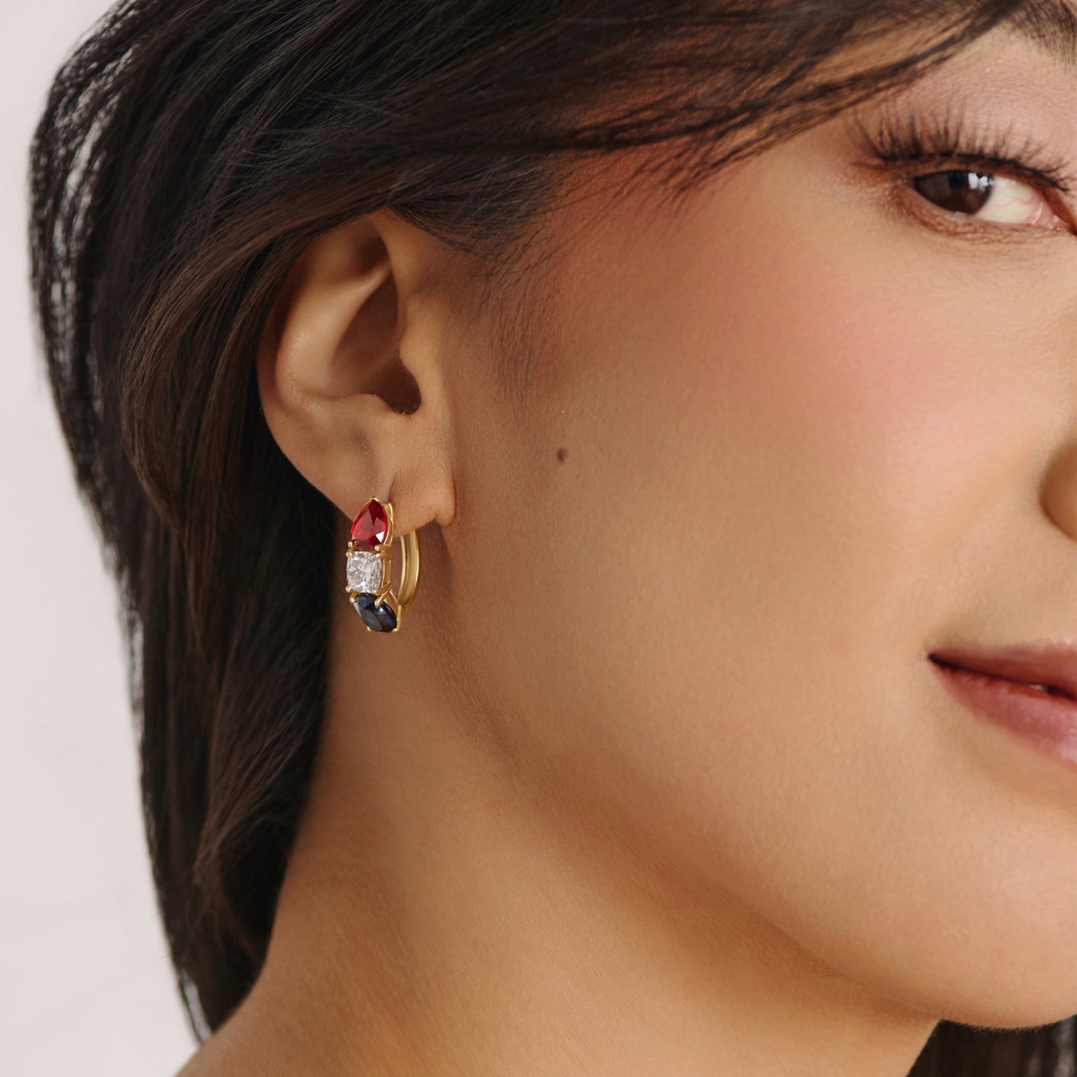 Model wearing solid white gold gemstone hoop earrings featuring red ruby, white diamond, and blue sapphire stones from the America250 fine jewelry collection.