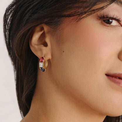 Model wearing solid white gold gemstone hoop earrings featuring red ruby, white diamond, and blue sapphire stones from the America250 fine jewelry collection.