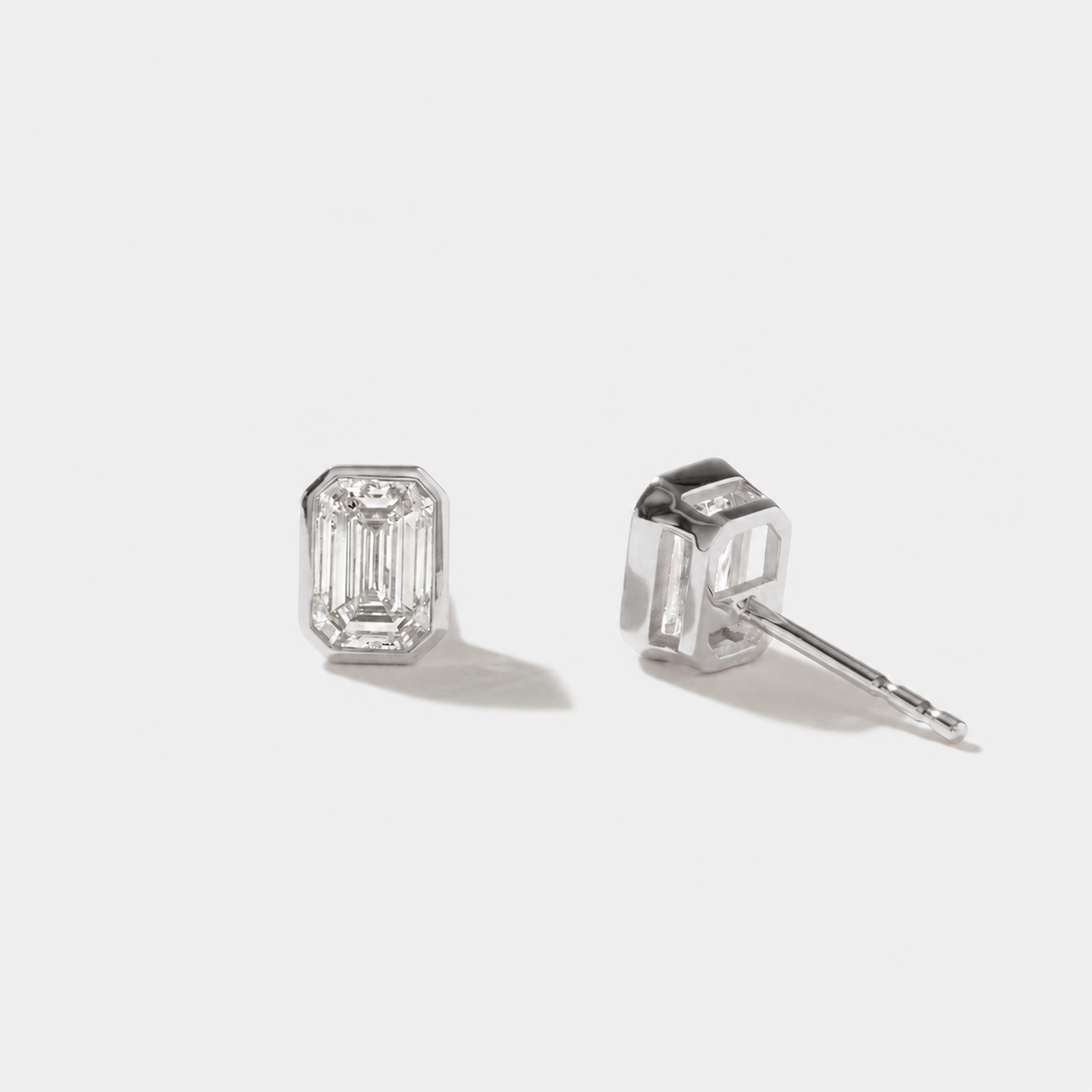 Emerald-cut diamond stud earrings in polished white gold bezel settings