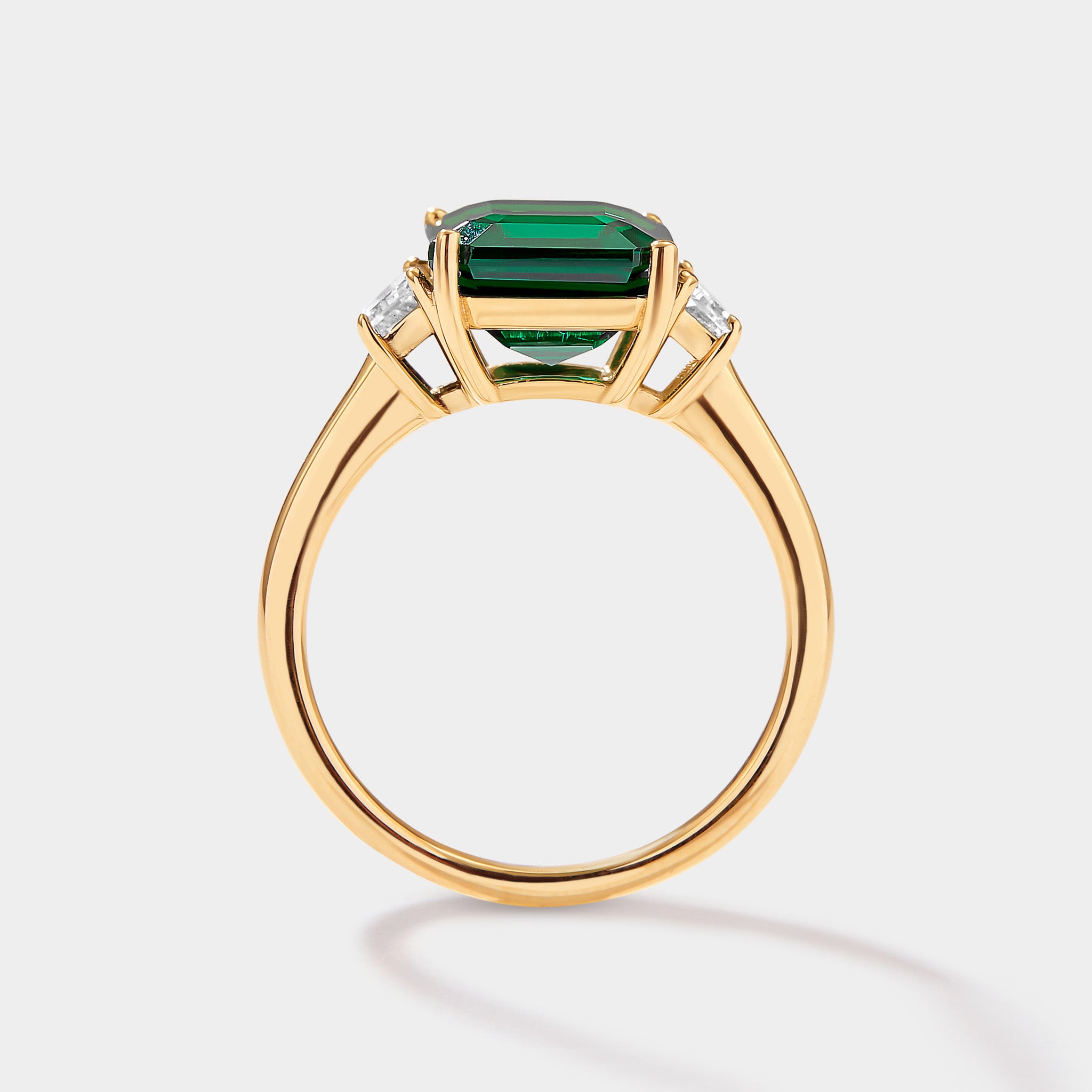 lab grown emerald three stone ring with emerald cut emerald and trapezoid diamonds