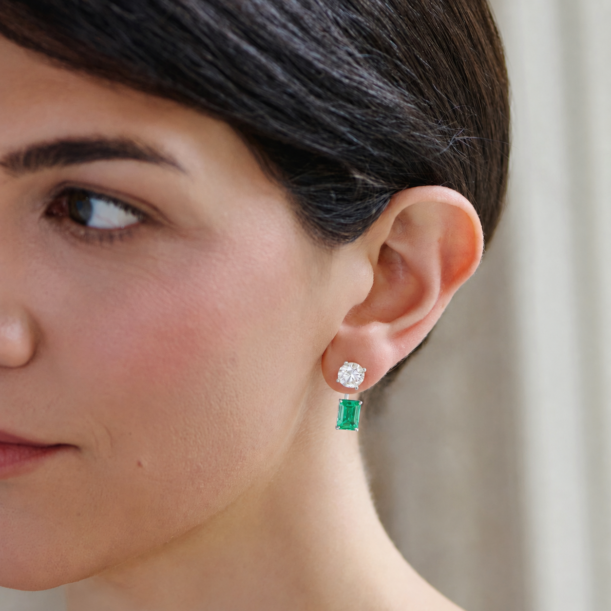 Model wearing lab-grown emerald earring jackets in white gold with round diamond stud earrings.