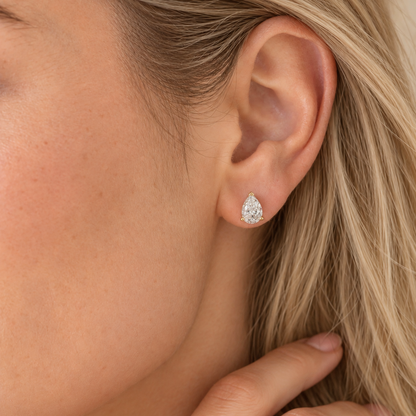 Model wearing a pear-shaped lab-grown diamond stud earring in a yellow gold three-prong setting.