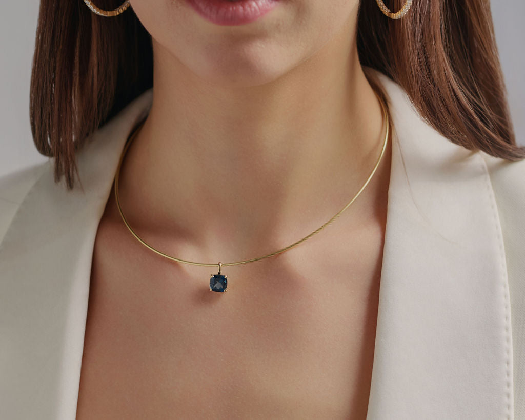Close-up of a London Blue Topaz pendant necklace on model, featuring a deep ocean-blue gemstone and lab-grown diamond details in solid gold.

